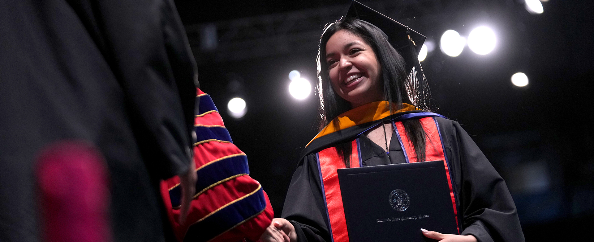 Graduate shaking hands with a faculty member as they cross the stage at commencement